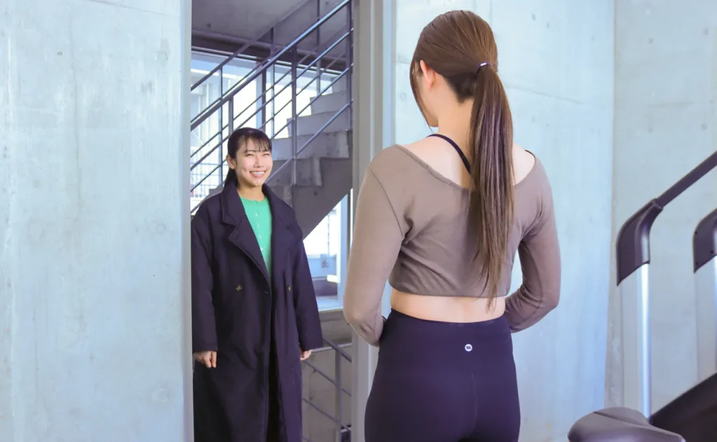 ピラティススタジオの入口で笑顔で出迎えるインストラクターと来店する女性