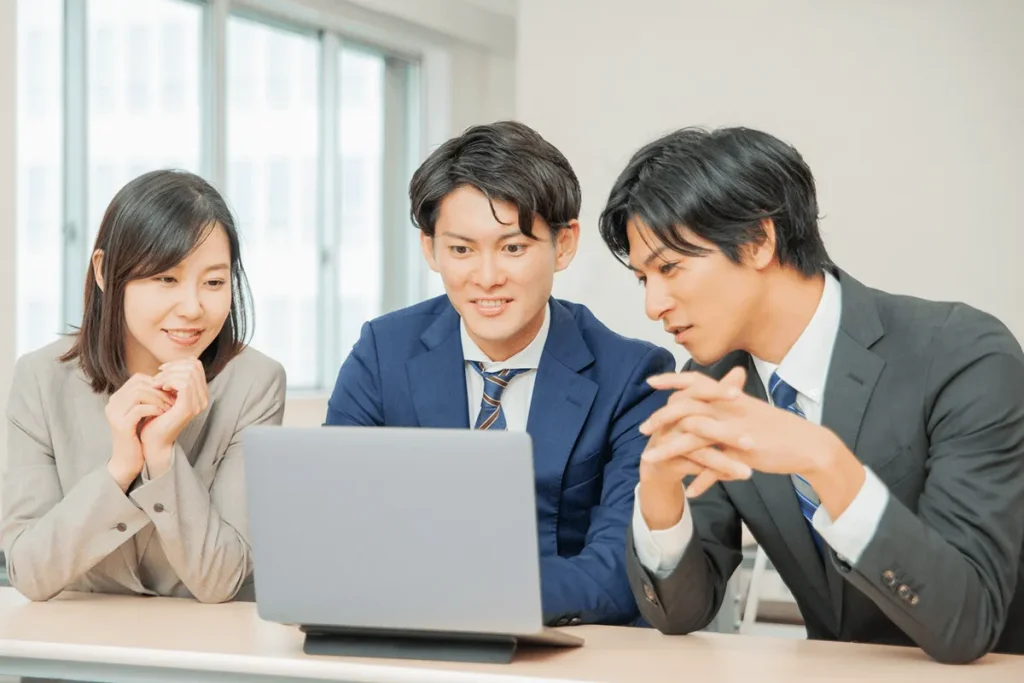 会議室でノートパソコンの画面を見ながら意見交換をするビジネスチームの男女